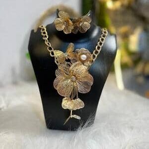 Intricate gold-tone floral statement necklace with matching flower earrings, featuring fine filigree metalwork and a pearl accent on a black display bust.
