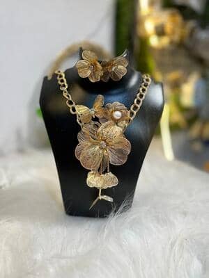 Intricate gold-tone floral statement necklace with matching flower earrings, featuring fine filigree metalwork and a pearl accent on a black display bust.