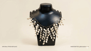 A handcrafted necklace featuring natural white oval stones on delicate gold-tone wire, displayed on a black jewelry bust with a clean beige background.