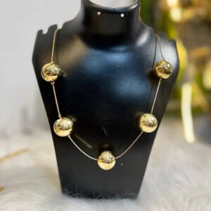 A modern necklace featuring five polished golden spheres on a delicate gold-tone wire, displayed on a black jewelry mannequin.